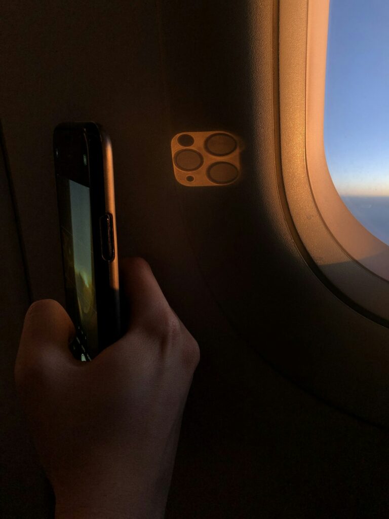 Passenger using smartphone with in-flight WiFi next to airplane window during flight